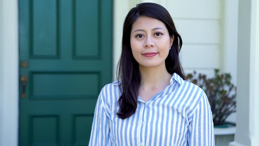 Professional woman outside in a neighborhood looking into the camera. asian young female real estate agent cross arms confident smiling standing in front the green door of white american style houese