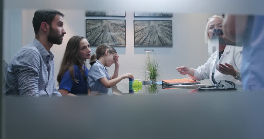 Slow motion shot of a doctor or specialist having conversation in clinic with parents about their autistic girls health. Doctor in hospital show little girl with aspergers lab test results to parents Royalty-Free Stock Footage #1020966457