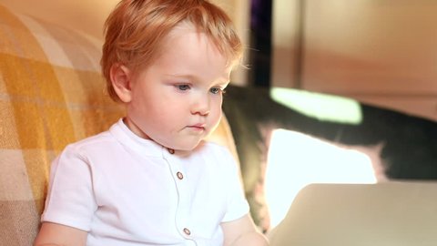 closeup portrait of serious blonde one year old baby boy using laptop computer indoors with sunlight on background happy childhood technology lifestyle internet technology modern device trend