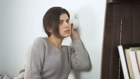 Young woman Use a cup and put it against the wall. He hear Through Wall what they're saying in another room.