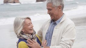 Attractive senior couple embracing eachother and smiling on beach in fall