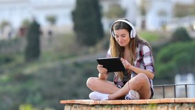 Happy teen listening and watching media content on a tablet sitting on a ledge on vacation