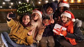 Multiethnic happy friends in warm clothes making selfie on smartphone in snow street