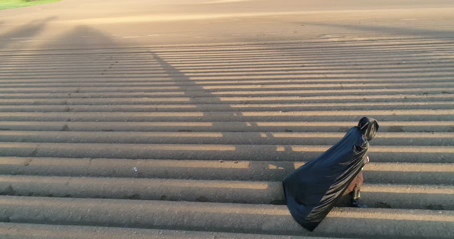Environmental protection. Death of nature. Apocalypse. Man dressed in black cape walks along the grey field towards the sun. Aerial view | Shutterstock HD Video #1020992194