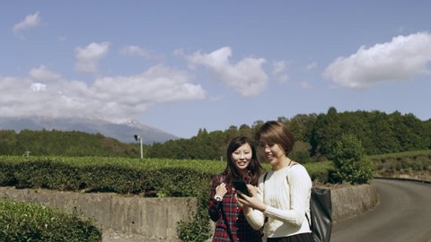 Two excited, happy Japanese women taking pictures together in a tea plantation with Mount Fuji in the background, with soft natural lighting. Wide to Medium shot on 4k RED camera.
