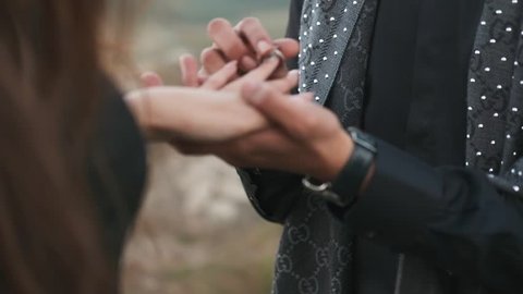 A Young Man Puts A Engagement Ring On The Finger Of A Woman And Kisses Her Hand With Love. Man Is Wearing Black Stylish Clothes. A Young Woman Made A Manicure With Long Nails, A Beautiful Pink Color