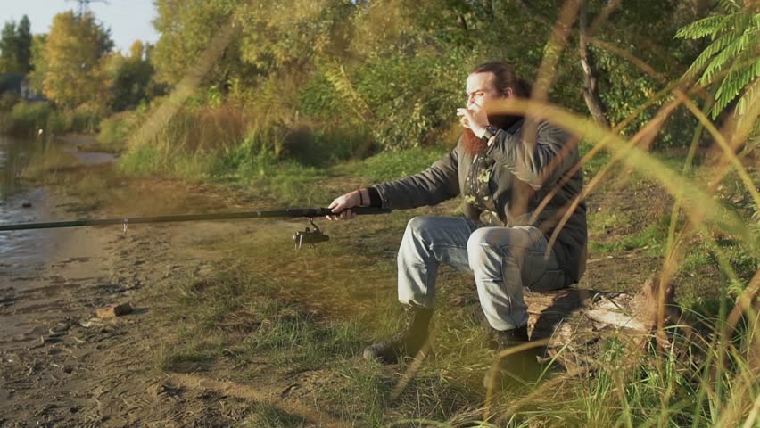 Bearded fisherman fishing on the river bank. Fisher gets up and tensely waiting for the fish to bite. River fishing.