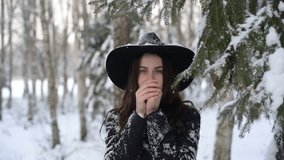 Charming,  happy and smiling girl in a hat poses by the tree in winter forest