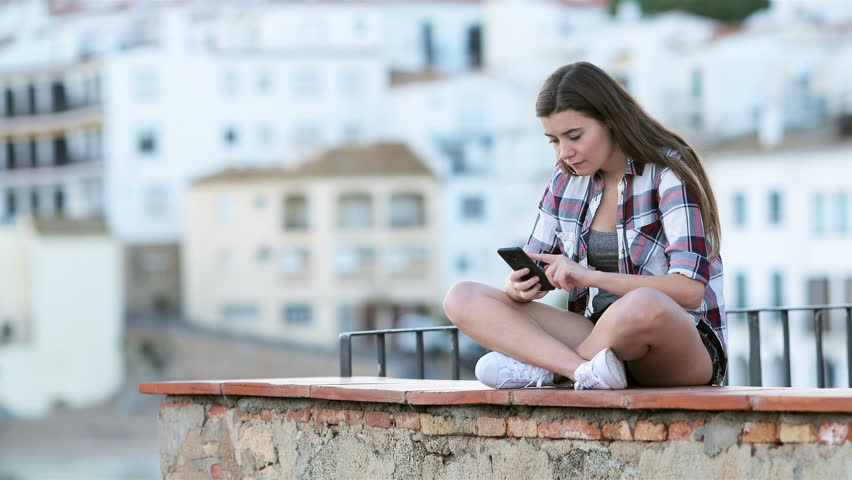 Sad teenage girl crying after reading text on a smart phone sitting on a ledge on vacation Royalty-Free Stock Footage #1020999829