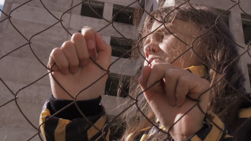 Frustrated child. Sad girl behind the iron fence.