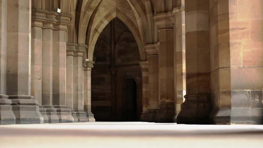 Optical Illusion. The Young Man Comes Out From Behind The Columns, Passes Along The Hall And Hides In The Wall Of The Columns. Tourist Walks Through The Old English Castle With A Lot Of Columns And