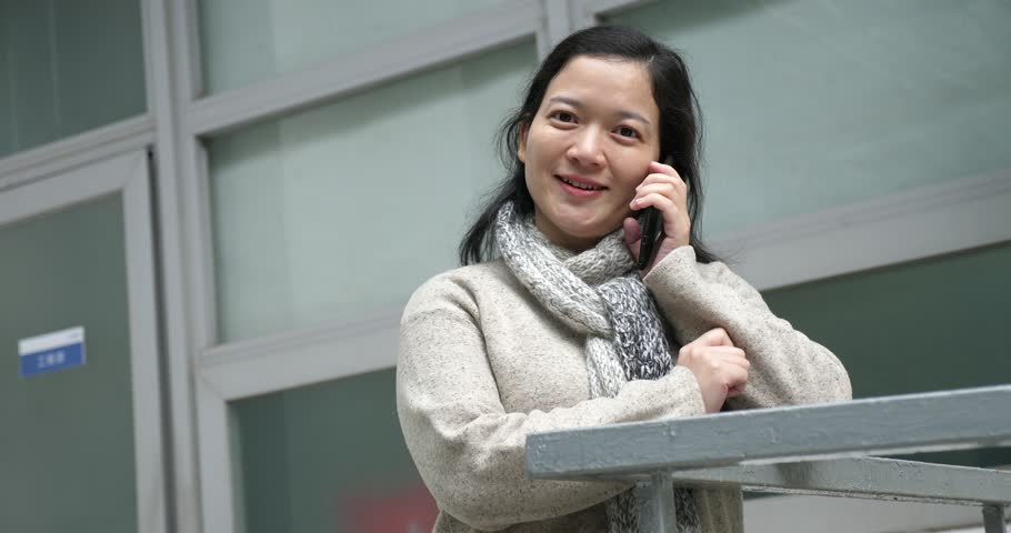 Chinese woman in sweater making a call on a mobilephone outside a building with smilling | Shutterstock HD Video #1021019152