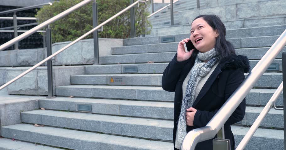 chinese woman in black coat making a call on a mobilephone on stairs