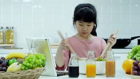 Little girl using tablet to assist him prepare healthy food at kitchen. Girl try to cooking by himself at home. People with healthcare and technology concept.