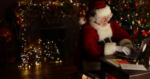 Santa Claus communicates through the headset with someone sitting at the table in a room decorated for Christmas. Christmas and New Year time.