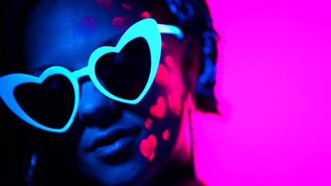 Portrait of fashion model woman with heart shaped glasses in neon light. Fluorescent unusual makeup glowing under UV light. Night club, party, halloween psychedelic concepts