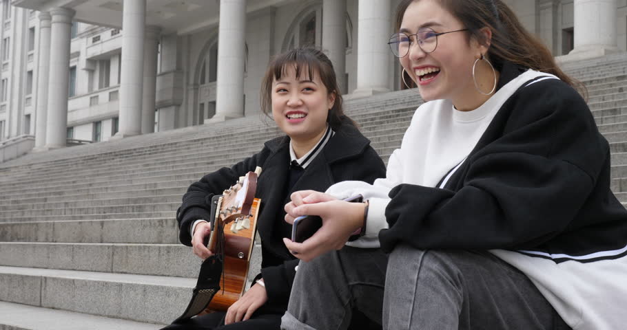 two young girls playing the guitar and singing together happily on steps with smilling