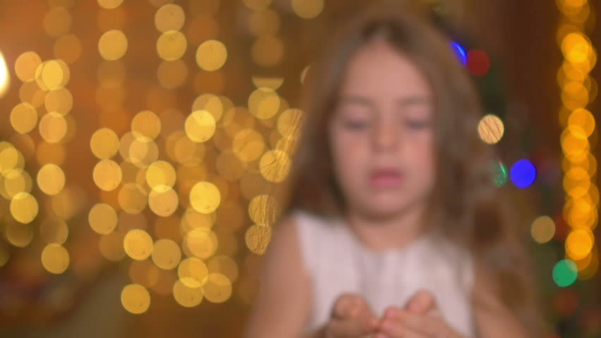 Holidays, a young girl blows from her hands colorful confetti, on the background of bright festive lights