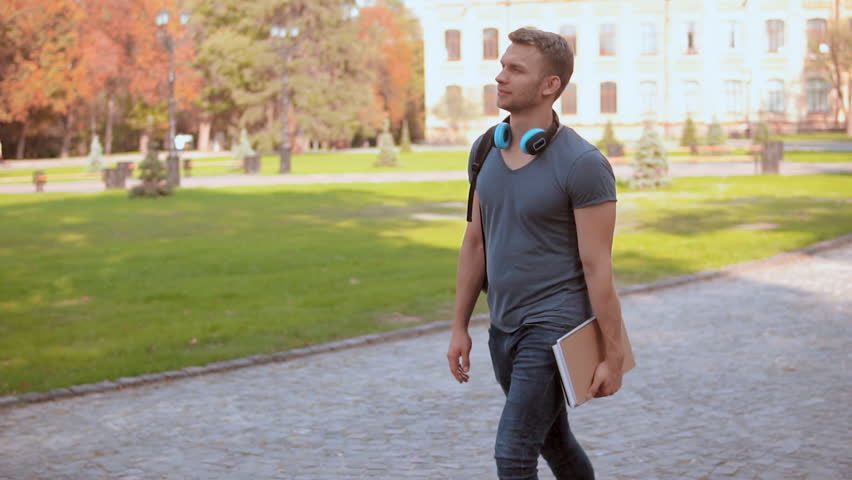 young handsome man with backpack holding notebook walking campus area view on beautiful nature autumn season slow motion Royalty-Free Stock Footage #1021070554