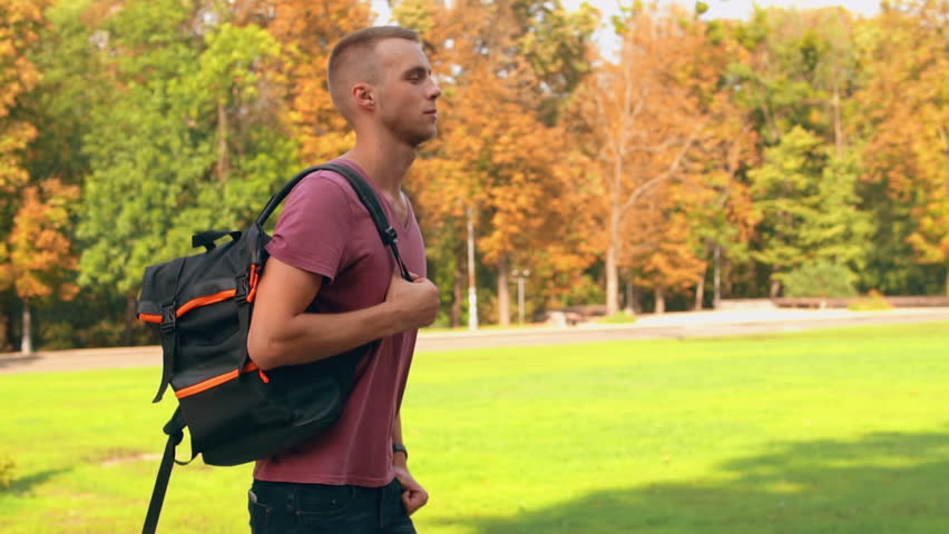young caucasian man with backpack walking in town view on beautiful nature autumn season slow motion