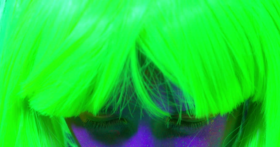 Closeup woman face with fluorescent make up in green, wig, creative makeup look great for nightclubs. Halloween party, shows and music concept - slow motion video