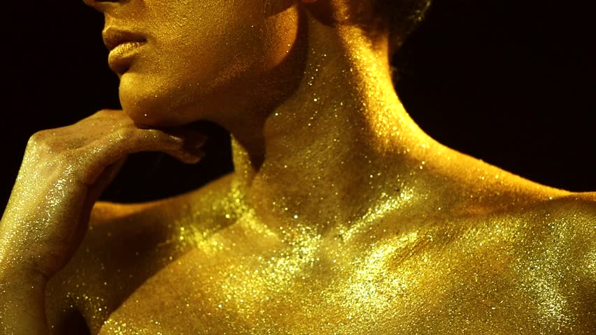 High Fashion model woman in golden bright sparkles posing in studio, portrait of beautiful sexy girl, trendy glowing gold skin make-up. Art design make up. Glitter metallic shine makeup 4K slow motion