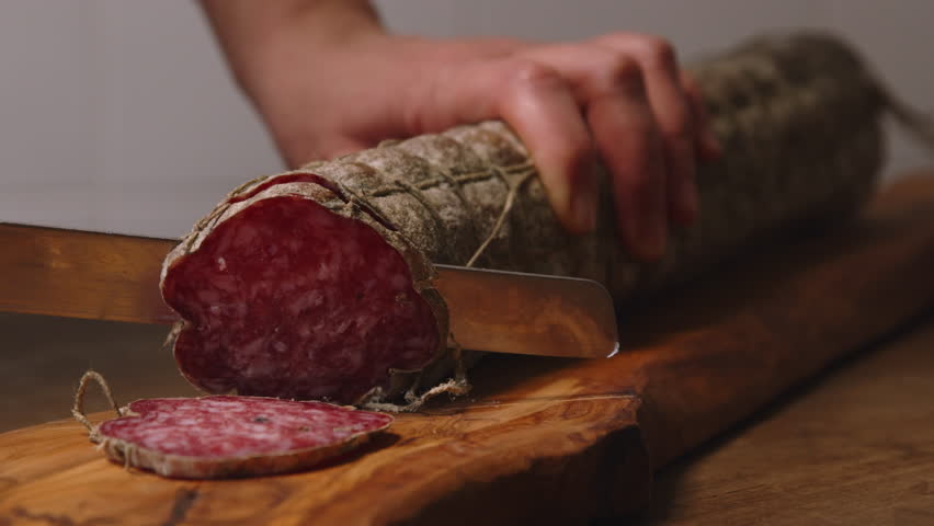A producer of salami is cutting a salami with a knife | Shutterstock HD Video #1021099345