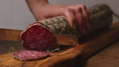 A producer of salami is cutting a salami with a knife