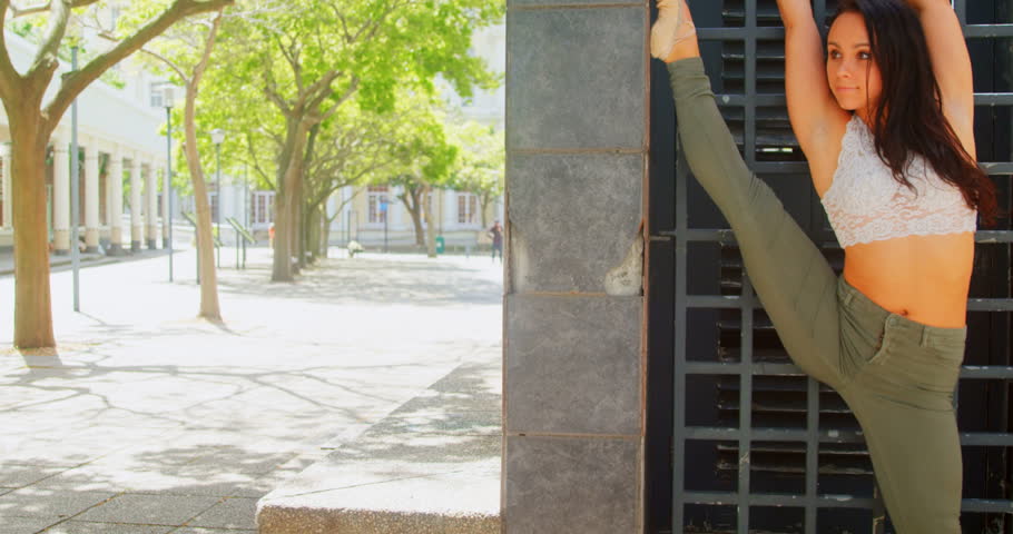 Front view of beautiful Caucasian female dancer stretching against wall grill in the city, Posing gracefully against the wall 