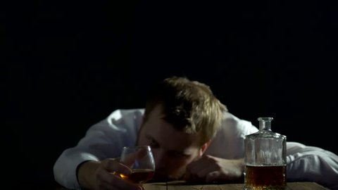 Sad male businessman with a beard looks at a bottle of alcohol, alcoholism, black background, problems