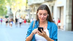 Front view of a girl choosing and listening to music from smart phone outdoor in the street