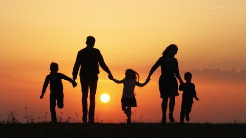 Silhouettes of family holding the hands and running in the meadow during sunset.