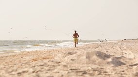 Person runs on the beach and seagulls fly off scared. Active sporty lifestyle concept video.