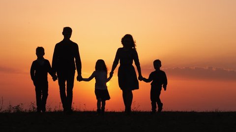 Silhouettes of happy family walking together in the meadow during sunset