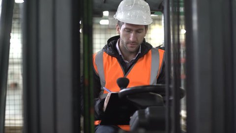 Concentrated forklift driver comes inside, checking the tablet inside machine.