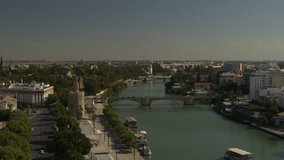 Panning aerial view of boat on urban river / Seville, Sevilla, Spain