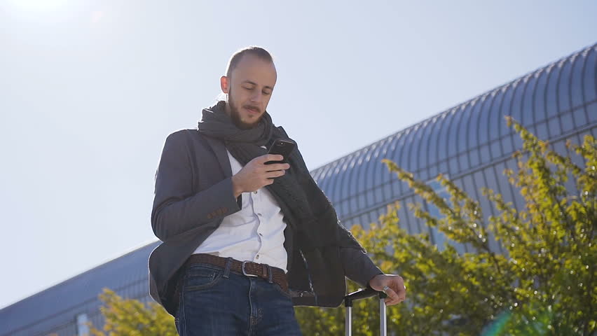 Caucasian businessman uses and talking on phone while he standing near the modern office building. Outdoors . Concept: office worker, business, business trip, advertising. Slow motion