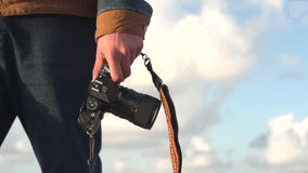 Low angle shot of man walking outside holding a camera leash looking for the perfect shot. Slow motion footage real life. Sunny day clouds at background. Close Up Of Skillful talented Photographer 