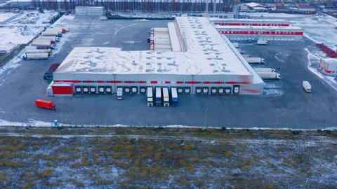 Aerial view of logistics warehouse center, loading dock with many semi-trailer trucks load/unload goods