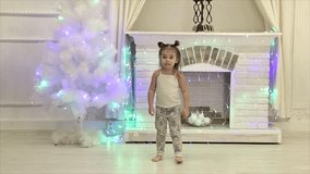 little girl with two tails dancing funny on the background of fireplace and Christmas tree