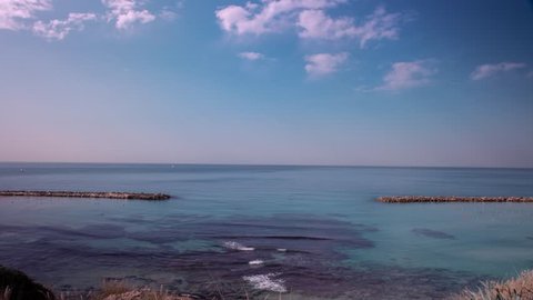 Time lapse of a mediterraenean beach, between 2 breakwaters. Shot in wide angle, on a bright day, with quiet waters and a bright sky with some white clouds crossing the frame.