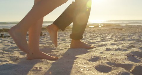 Low section of couple walking at beach on a sunny day. Couple walking barefoot 4k