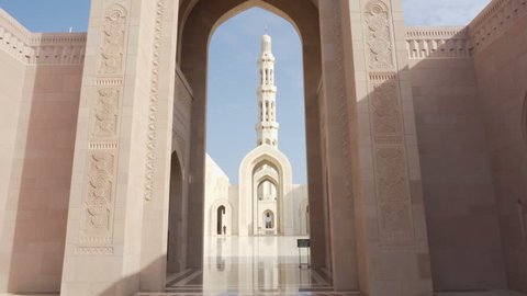 Beautiful view of arches at courtyard of the Sultan Qaboos Grand Mosque in Muscat, Oman. Amazing white marble floor. Wonderful minaret is visible on blue sky background. Scenic Islamic architecture.