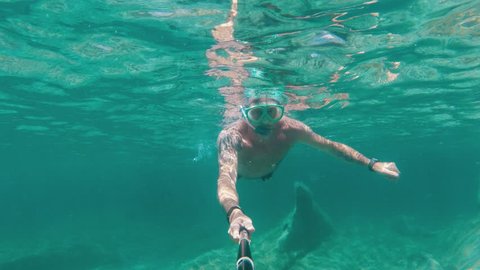 Caucasian man with a mask and snorkel swimming under water with a selfie stick, action camera footage