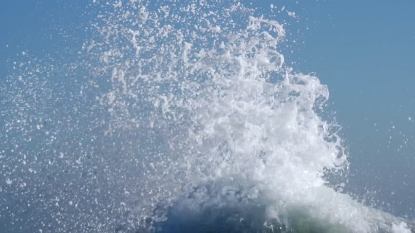 Splashes large strong waves on pier against background of bright blue sky on spring sunny day slow motion. Approaching wave with splashes of water. Strength and power of breaking wave on pier. Splash