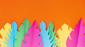 Tropical colored paper leaves dancing on an orange background. Stop motion animation.