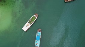 Drone footage of ships in Halong Bay, Vietnam. Green water and a sip on a boat trip in Ha Long Bay, Vietnam. People are swimming in the water.