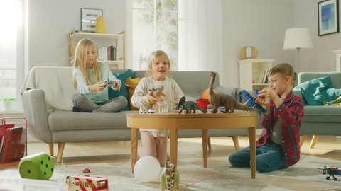 At Home: Cute Girl Playing in Video Game Console, Using Joystick Controller, Her Younger Brothe Plays with Toy Airplane and Youngest Sister Plays with Toy Dinosaurs. Happy Children Playing?