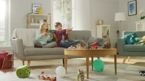 At Home: Smart Boy Playing in Video Game Console, Using Joystick Controller, His Older Sister Sits Near on Sofa and Cheers for Him. They Win and Celebrate Happily. Happy Children Playing Videogames.