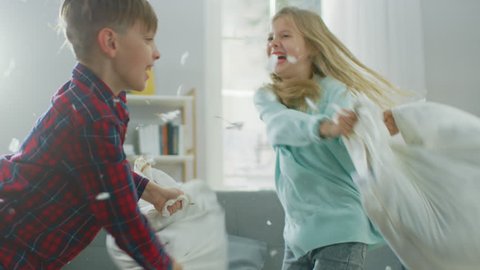 Adorable Little Boy and Sweet Little Girl Have a Pillow Fight in the Sunny Living Room. Siblings Having Fun Fighting with Pillows, Feathers Flying Around. In Slow Motion